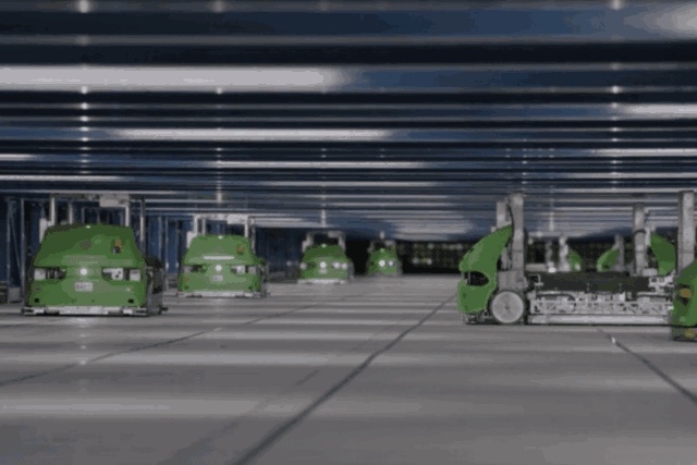 Green robots sorting parcels in a futuristic automated warehouse environment with stacked shelves in the background.