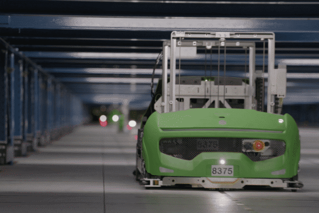 Autonomous green vehicle moving in an indoor facility with artificial lighting.