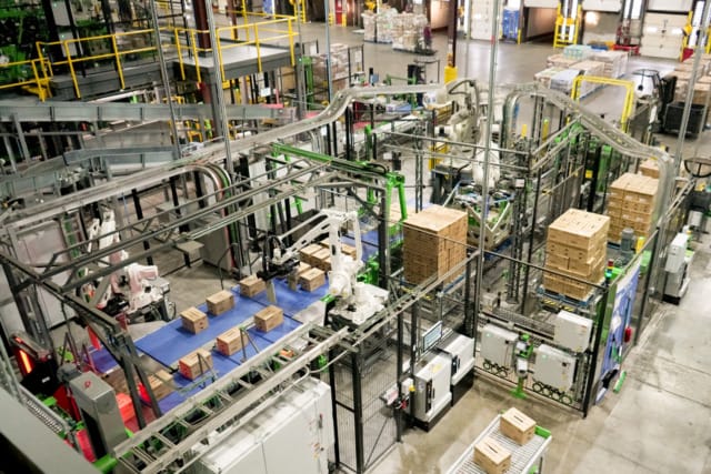 Overhead view of an automated industrial facility with robotic arms handling boxes on conveyor belts.